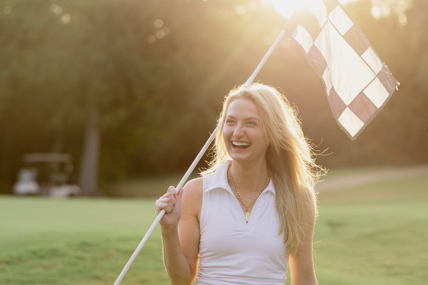 Late sun on the green, a checkered flagstick over one shoulder, mid-laugh.